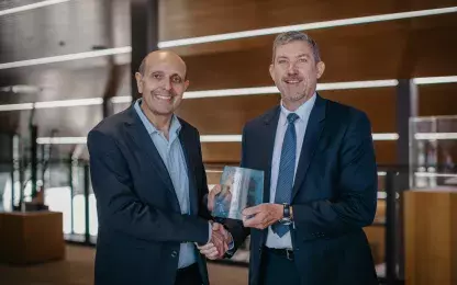 two men standing in a room shaking hands and holding a trophy