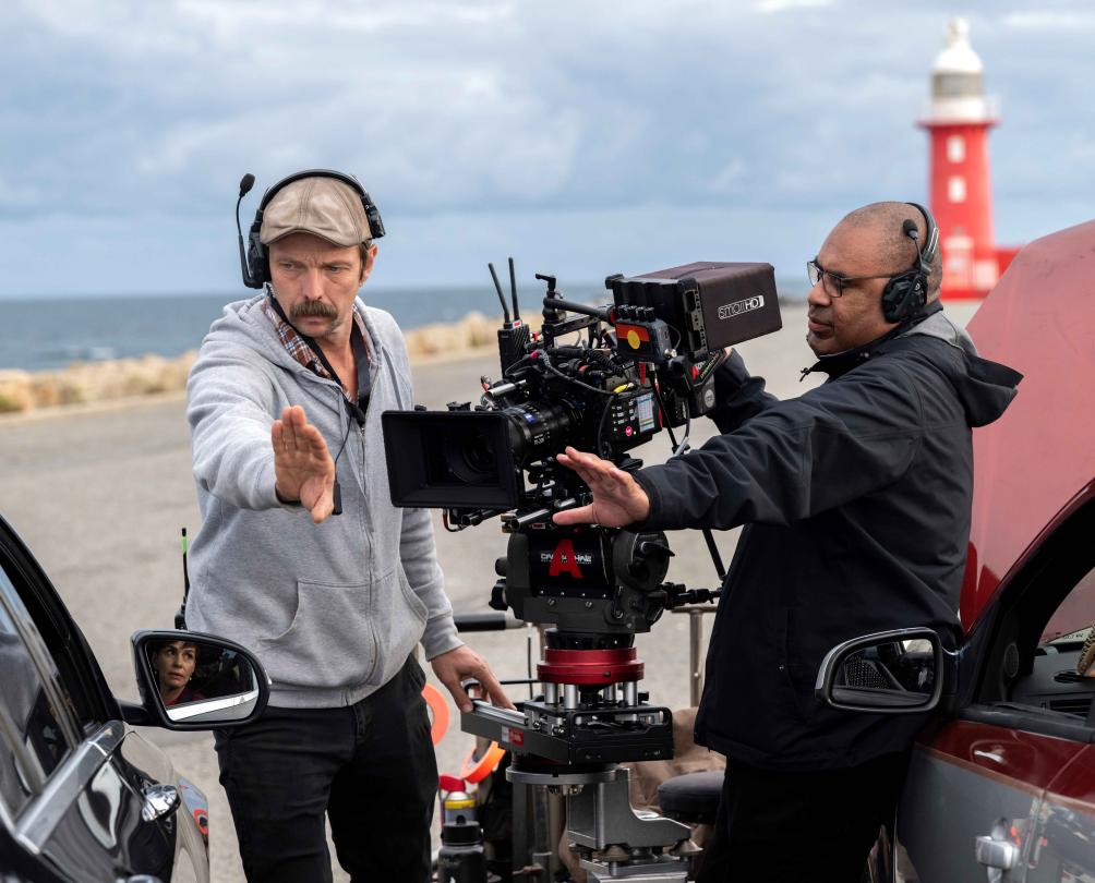 a director and a film crew standing on south mole with a lighthouse in the background